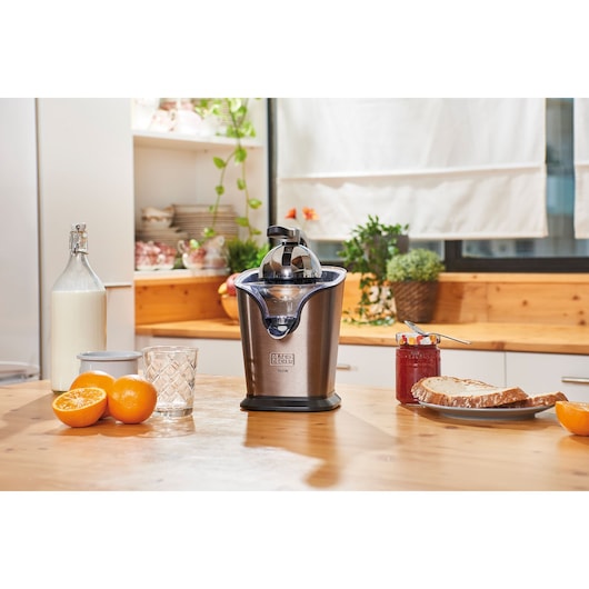 Photo of BLACK+DECKER BXCJ100E stainless steel citrus juicer on a kitchen table beside oranges, glass, and breakfast items.