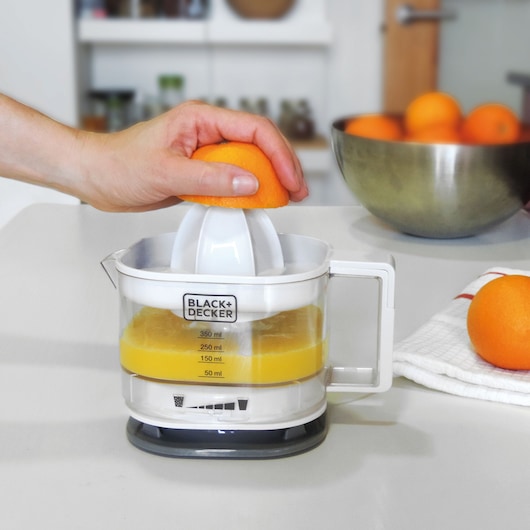 BLACK+DECKER BXCJ25E electric citrus juicer with hand pressing orange in kitchen setting.