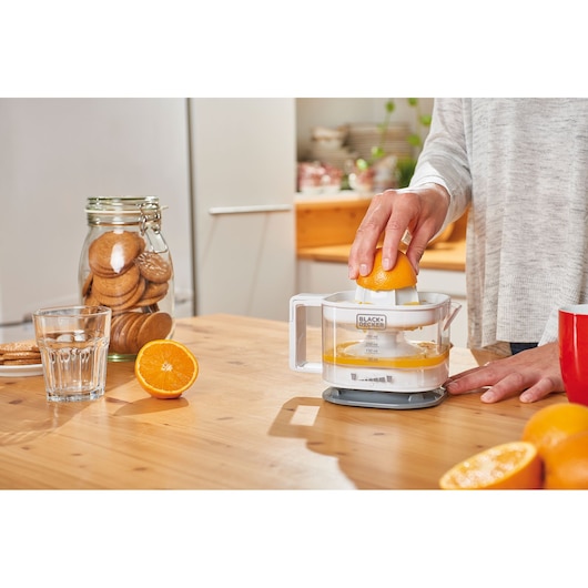 BLACKDECKER BXCJ25E citrus juicer in use, tabletop, fresh oranges and cookies in kitchen background.
