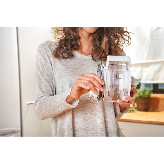 Person holding BLACK+DECKER BXCJ25E electric citrus juicer with transparent container and white lid in kitchen.