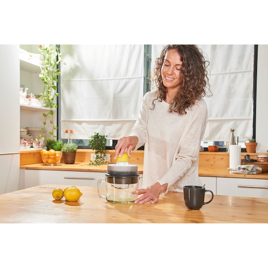 BLACKDECKER BXCJ30E citrus juicer on kitchen counter with lemons and mug, person using it.