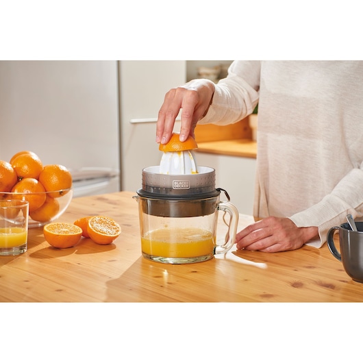 BLACKDECKER BXCJ30E citrus juicer in use on kitchen table with fresh oranges and glass of juice.