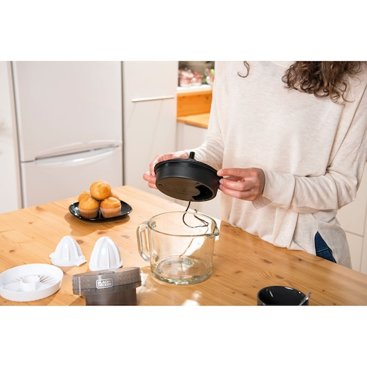 BLACKDECKER BXCJ30E electric citrus juicer with glass jug and accessories on kitchen table, person assembling lid.