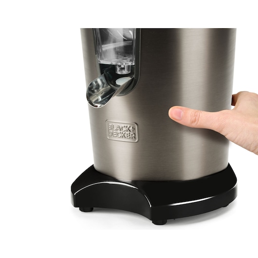 Close-up view of a BLACK+DECKER stainless steel juicer, with a person's hand pressing on the side of the appliance.