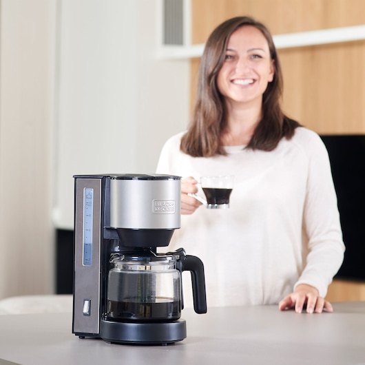 BLACKDECKER BXCO870E drip coffee maker in silver and black on kitchen counter, person holding a coffee cup.