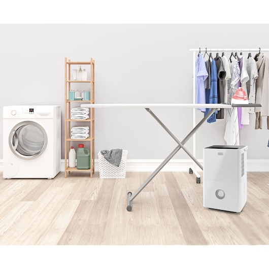 BLACKDECKER BXDH20E dehumidifier in a laundry room with ironing board, washing machine, and clothes rack.