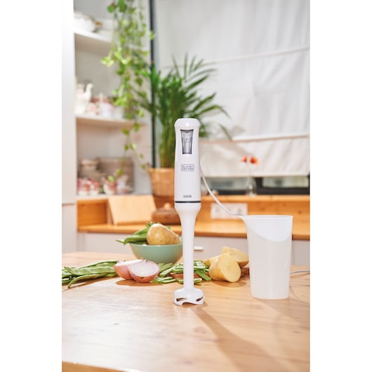 BLACKDECKER BXHB500E hand blender with mixing cup on kitchen table, vegetables in background.