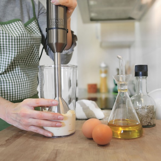BLACKDECKER BXHBA1000E hand blender mixing ingredients in glass, eggs and oil on kitchen counter.