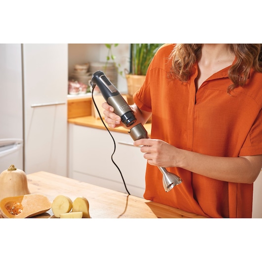 BLACKDECKER BXHBA1000E hand blender in kitchen, woman attaching blending shaft, vegetables on wooden table.