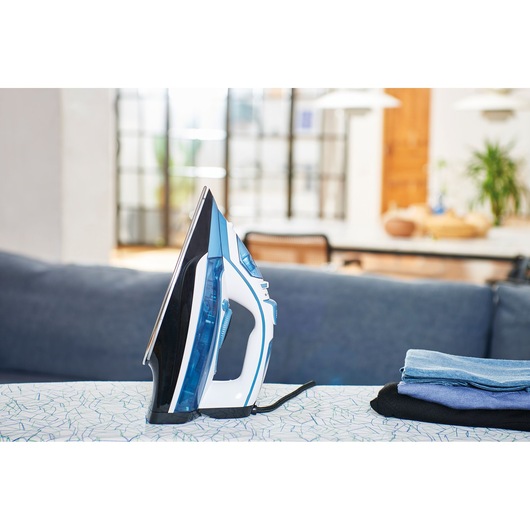 BLACK+DECKER BXIR2400E steam iron with blue and white body on ironing board, side view, next to folded clothes.