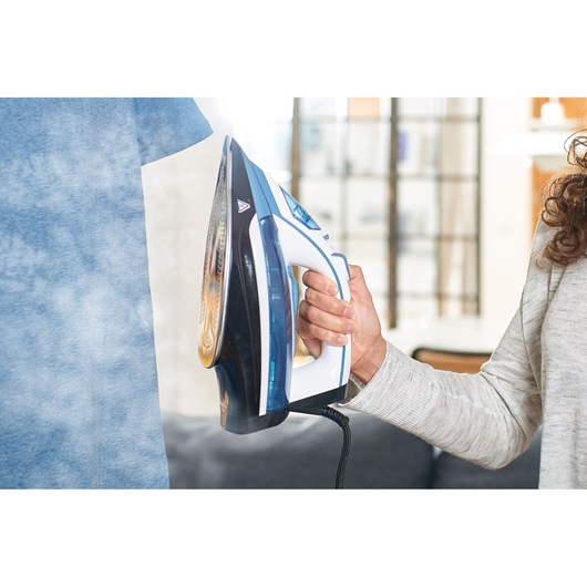 BLACKDECKER BXIR2400E steam iron in use, blue and white, steaming a blue shirt indoors.