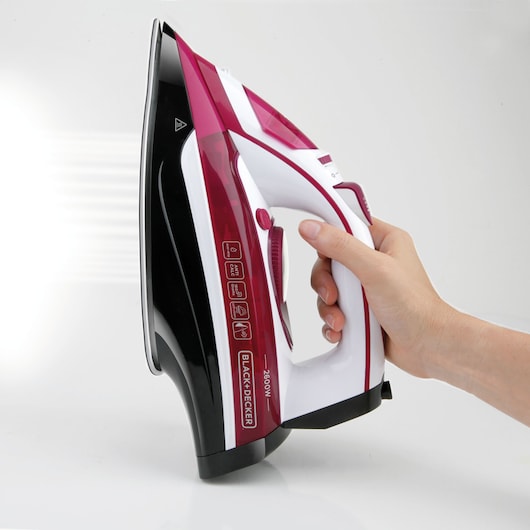 BLACK+DECKER BXIR2600E steam iron in white and magenta, side view, held by a hand, visible steam effect.