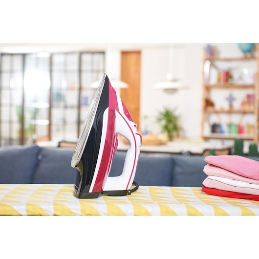 BLACKDECKER BXIR2600E steam iron with pink and white accents on ironing board, household setting.