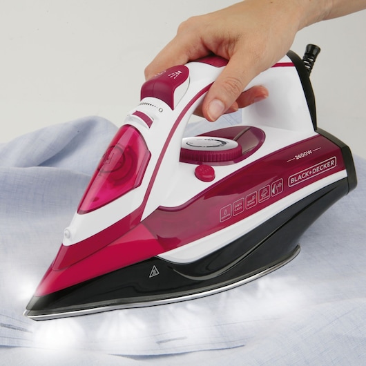 BLACK+DECKER BXIR2600E steam iron in red and white, pressed on fabric, photographed from side angle.
