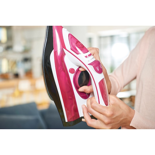 BLACKDECKER BXIR2600E steam iron in pink and white held in hand, close-up view.