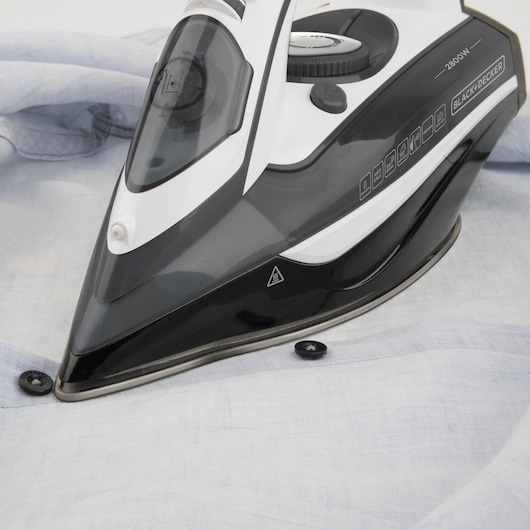 Photo of BLACKDECKER BXIR2800E steam iron on a light blue shirt, close-up angle.