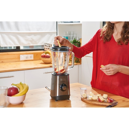 BLACKDECKER BXJB800E blender with glass jar, fruits being added, in a kitchen setting.