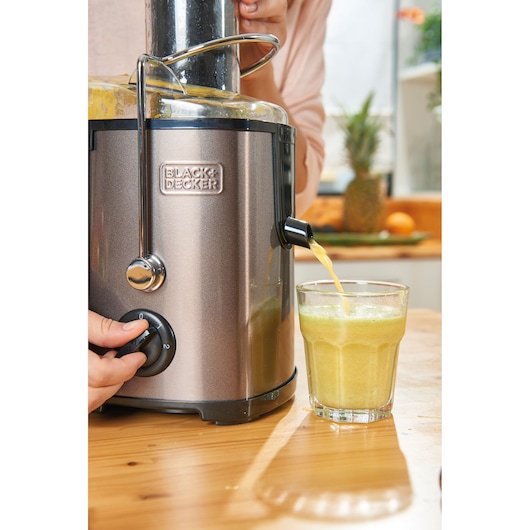 BLACKDECKER BXJE600E juicer pouring fresh juice into a glass on a wooden table in a kitchen.