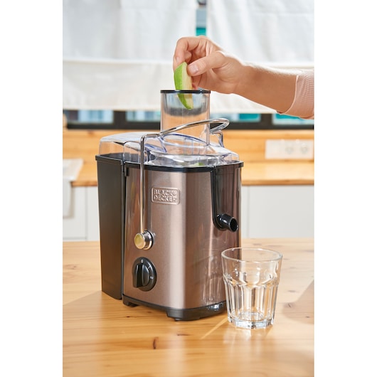 Photo of BLACK+DECKER BXJE600E juicer in kitchen, hand adding green apple slice, glass positioned at spout.