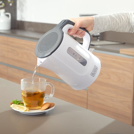 BLACKDECKER BXKE2200E white electric kettle pouring water into cup for tea on kitchen counter.