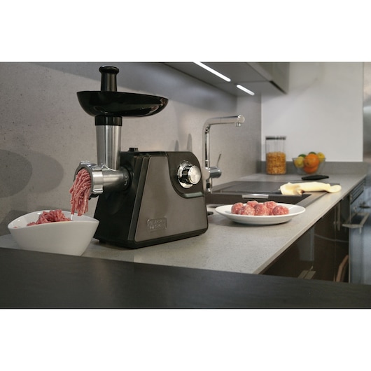 BLACKDECKER BXMM1000E meat grinder on kitchen counter, grinding meat into bowl, plate of meatballs nearby.