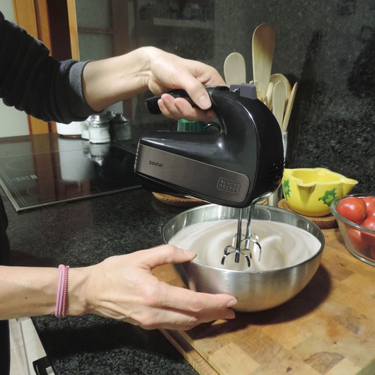 BLACKDECKER BXMX500E hand mixer mixing cream in a stainless steel bowl on a kitchen counter.