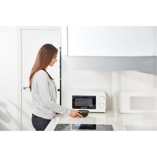 Photo of a woman using a BLACK+DECKER BXMY700E microwave oven on a kitchen counter.