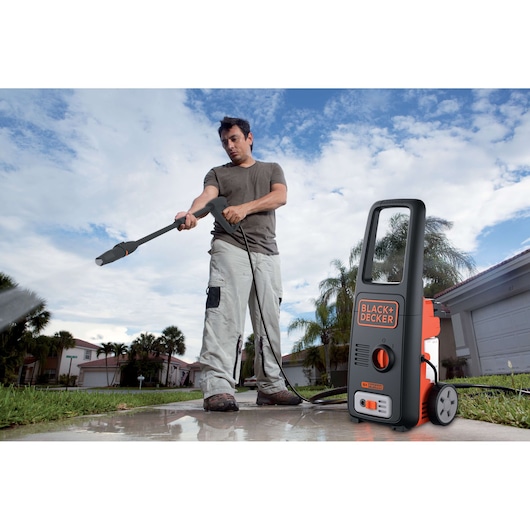 BLACK+DECKER BXPW1400E pressure washer used outdoors on wet pavement in front of a house, with palm trees visible.