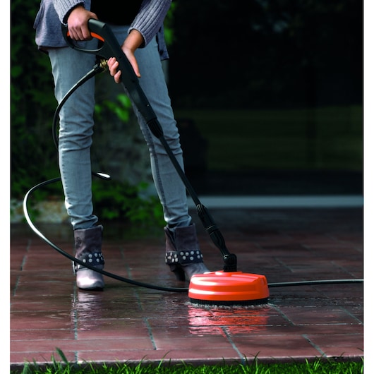 BLACKDECKER BXPW1400PE pressure washer being used to clean outdoor tiles with orange surface attachment.