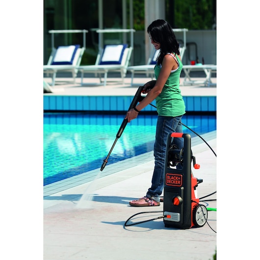 BLACK+DECKER BXPW1800E pressure washer cleaning poolside concrete, photo shows product in outdoor use.