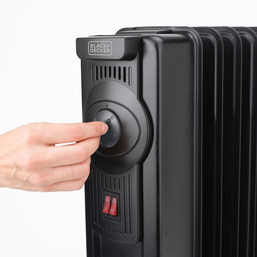 Photo of BLACK+DECKER BXRA1500E black radiator heater front angle, hand turning temperature dial.