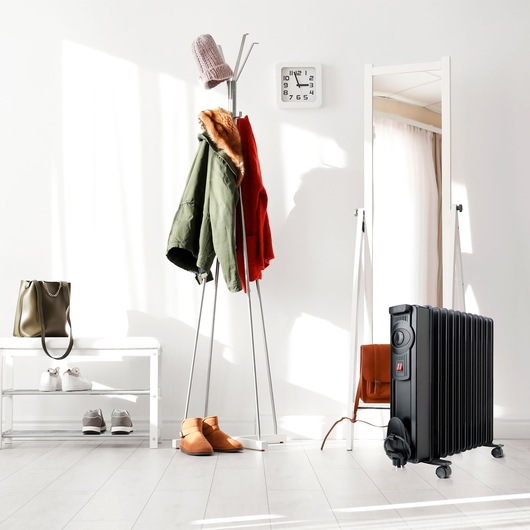 BLACKDECKER BXRA2000E black radiator heater in a modern entryway, near coat rack and mirror.