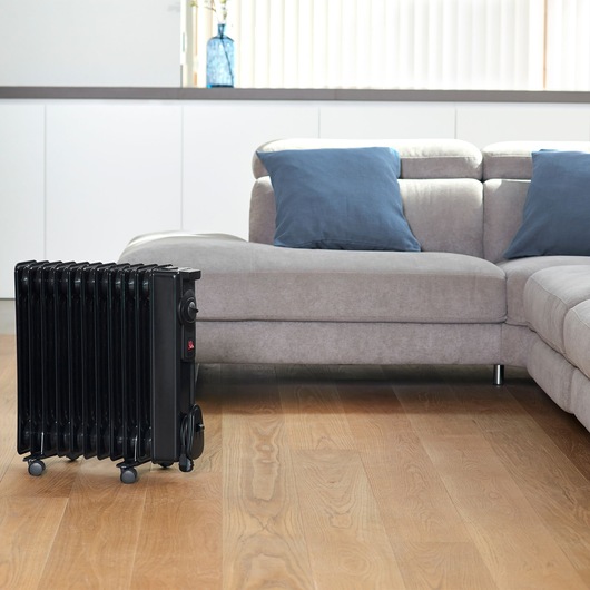 BLACKDECKER BXRA2000E portable black radiator heater on wheels in living room near grey sofa.