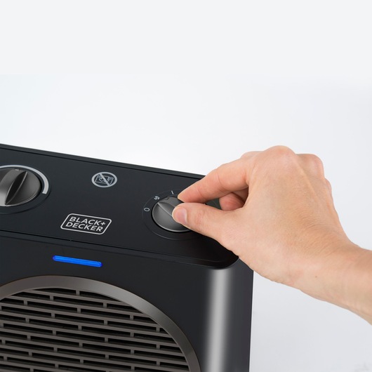 Photo of hand adjusting BLACK+DECKER BXSH1500E black portable heater control dial, close-up angle.
