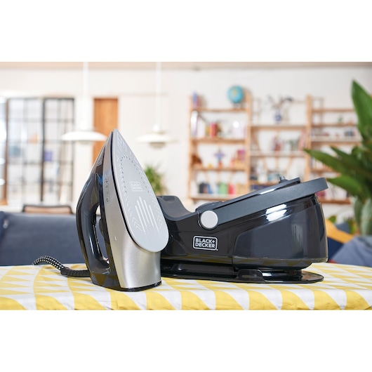 BLACKDECKER steam iron BXSS2200E with base, silver and black, on patterned tablecloth in a home setting.