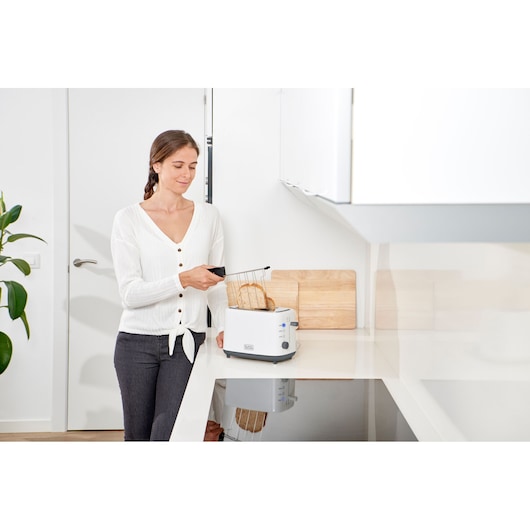 Person using BLACK+DECKER BXTOA820E toaster in modern kitchen with two slices of bread.