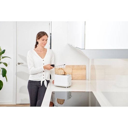 Photo of BLACKDECKER BXTOA820E white toaster on kitchen counter with two slices of bread and a person using it.