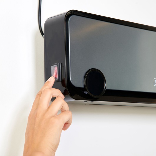 Photo of BLACKDECKER BXWSH2000E wall-mounted heater with hand pressing the power switch, front angle.