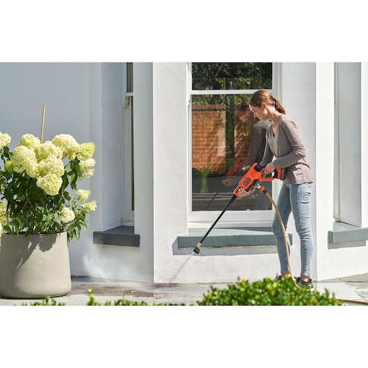 BLACK+DECKER BZO51N1 cordless pressure washer used outdoors to clean a patio near a white wall and potted plant.