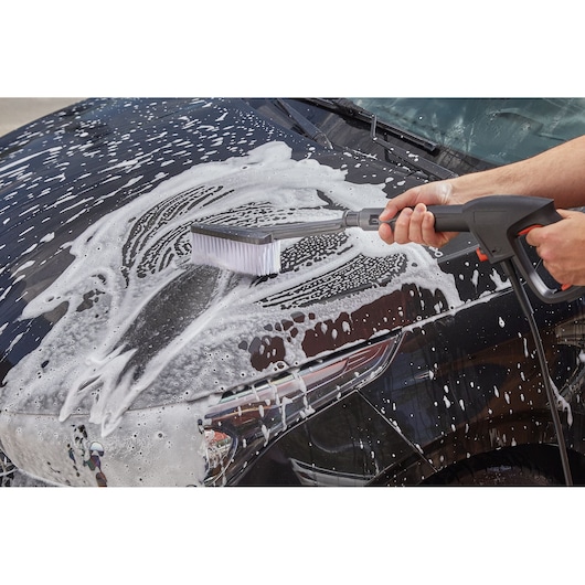 BLACK+DECKER BZOBR1-LA car cleaning brush spraying soap on black car hood, front angle.