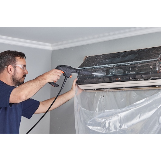 BLACKDECKER BZOSG1-LA steam cleaner used to clean a wall-mounted air conditioner unit, spray action visible.