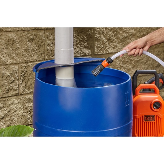 BLACKDECKER BZOSPK1 photography of orange water pump near blue barrel with hose beside stone wall.