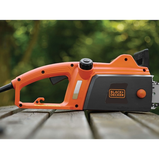 Photo of BLACK+DECKER CS1835 electric chainsaw, side view, orange and black housing, on a wooden surface outdoors.