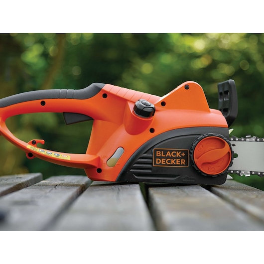 BLACKDECKER CS2040 orange and black electric chainsaw partial side view on a wooden surface outdoors.
