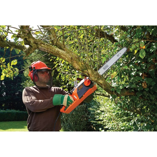 BLACKDECKER CS2245 chainsaw in use cutting tree branch outdoors, orange and black body, garden setting.