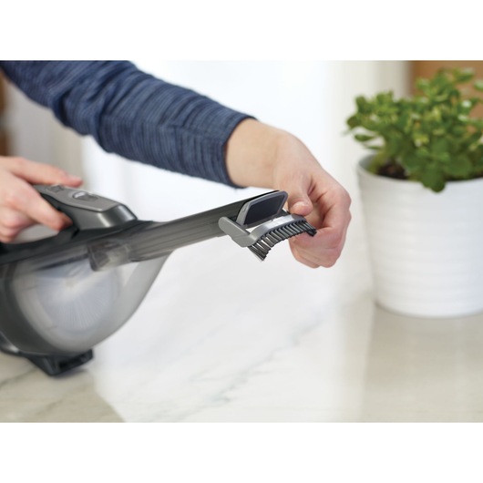 BLACKDECKER DVA320J handheld vacuum with brush attachment on countertop, plant in background.