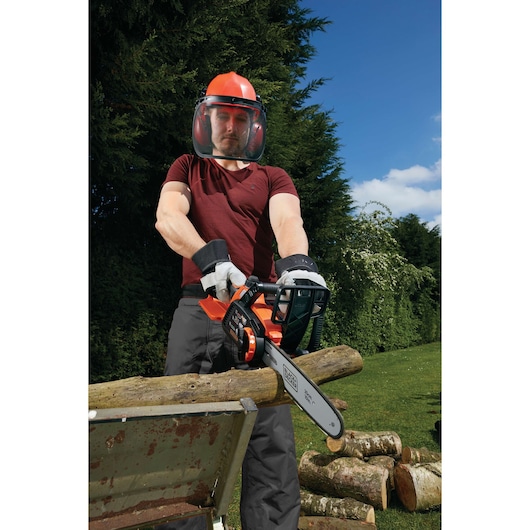 Photo of BLACK+DECKER GKC1825L20 chainsaw in use, cutting logs outdoors, user wearing safety gear.