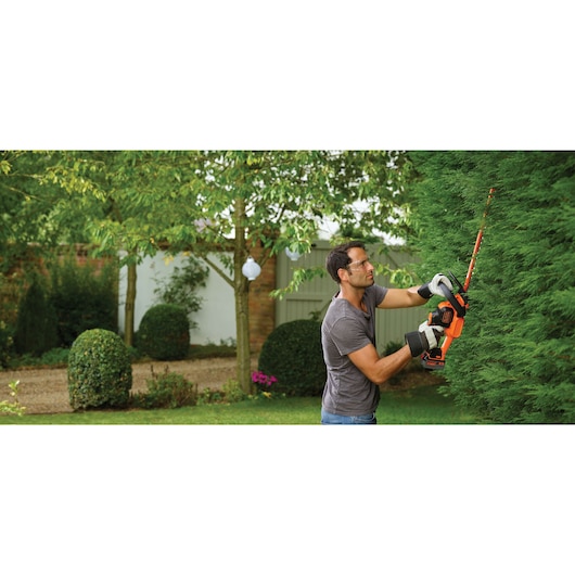 BLACKDECKER hedge trimmer GTC18504PC in use, orange and black tool trimming green hedge outdoors.