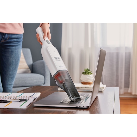 BLACKDECKER HLVC315B11 handheld vacuum cleaning a laptop keyboard on a desk in a living room.