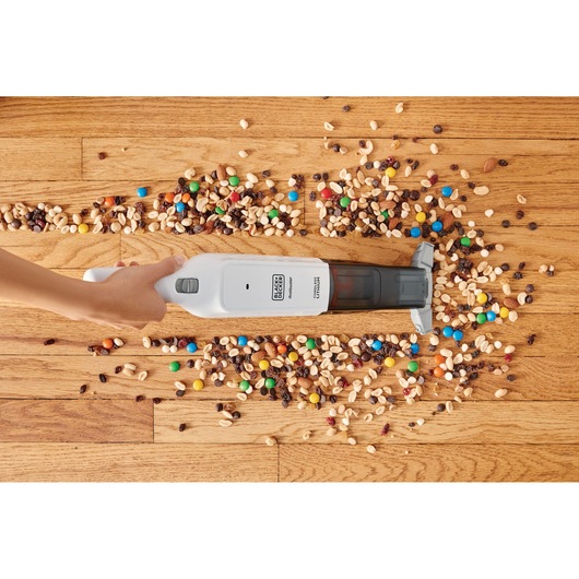 Photo of BLACKDECKER HLVC315J11 handheld vacuum cleaning mixed snacks from wood floor.